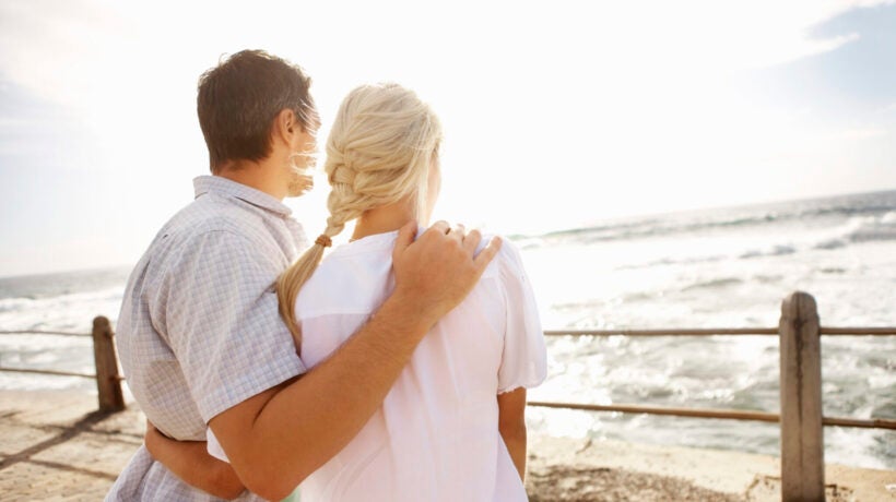Rear view of young couple with arms around enjoying the view on the beach