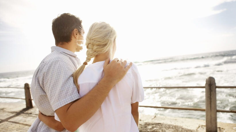 Rear view of young couple with arms around enjoying the view on the beach