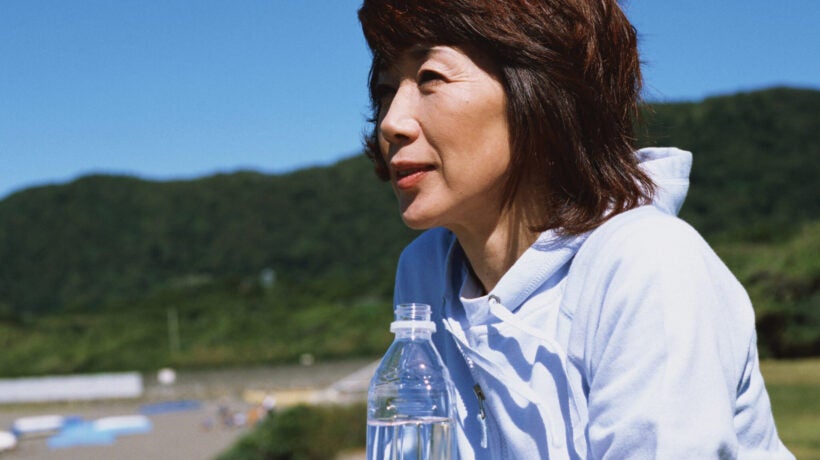 Asian woman leaning on a railing while holding a bottle of water